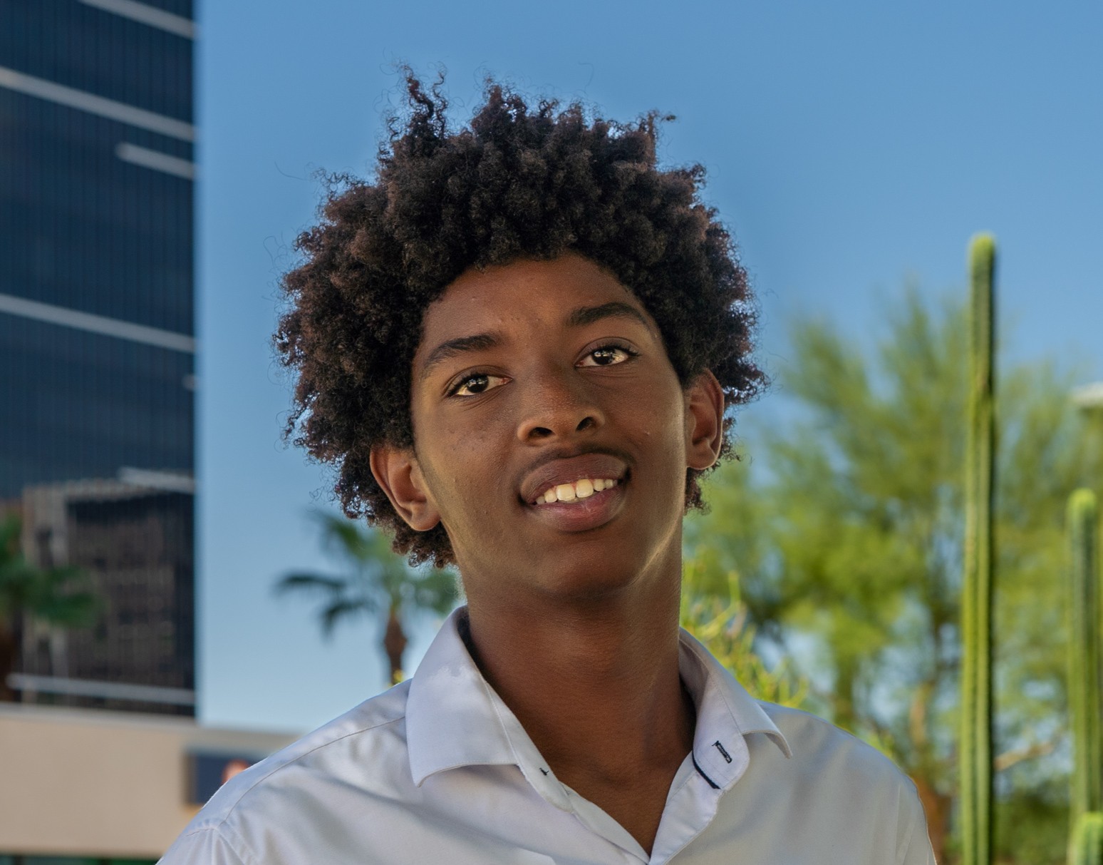 Isaiah smiling with tree/ cactus and building in background