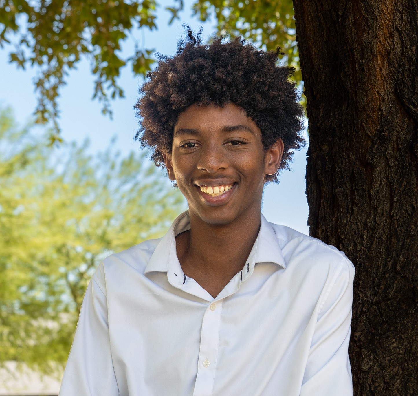Isaiah smiling leaning against a tree