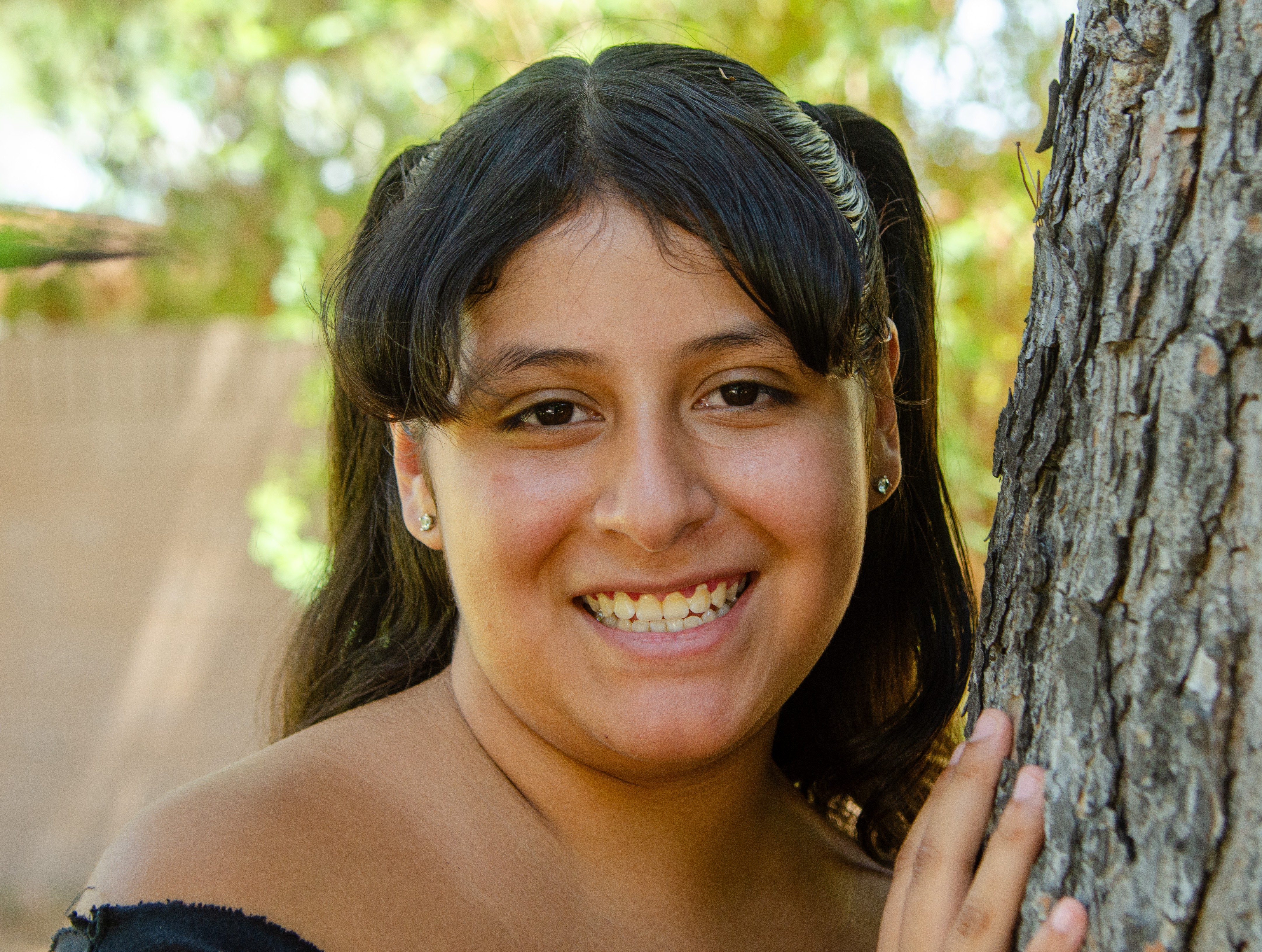 Destiny smiling leaning on a tree.
