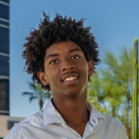 Isaiah smiling with tree/ cactus and building in background