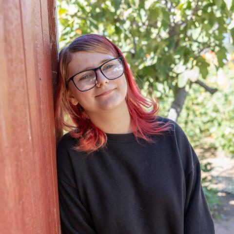 Kaylyn leaning against wall with tree in background